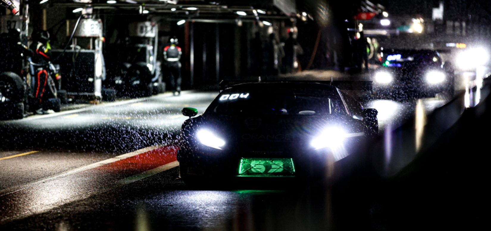 Racing cars in a dark and rainy pitlane in the Fanatec GT World Challenge Powered by AWS